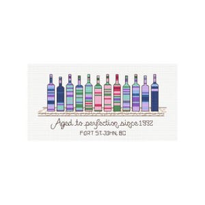May include: A cross-stitch pattern featuring twelve colorful bottles arranged in a row, each with unique horizontal striped designs. Below the bottles, the text reads Aged to perfection since 1992 and Fort St. John, BC, in black lettering.