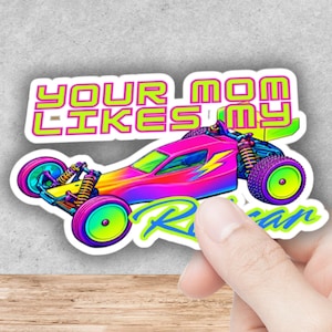 Op de afbeelding: Een gestanste sticker met een levendige, meerkleurige op afstand bestuurbare raceauto met een neonroze, gele en blauwe gradiënt carrosserie. De tekst "YOUR MOM LIKES MY RACE CAR" staat in dikke, felgroene en roze letters boven en onder de auto.