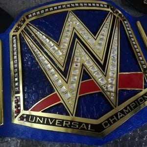 May include: A blue and gold championship belt with the text "UNIVERSAL CHAMPION" and the WWE logo. The belt has a blue leather strap and is decorated with rhinestones.