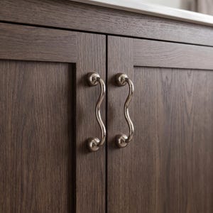 May include: Two vertical cabinet doors made of dark brown wood with a visible grain pattern. Each door features a polished silver-toned metal handle with a distinct wavy, serpentine shape, secured by two circular mounting plates at each end.