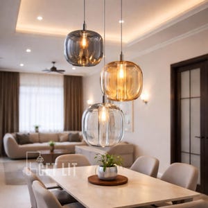 May include: Three pendant lights with rounded, clear glass shades hang above a dining table. The shades have a pumpkin-like shape and contain a warm, glowing light. The lights are suspended from the ceiling in a modern dining room setting.