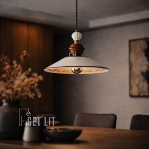 May include: A pendant light fixture with a white lampshade and a brown wooden base. The light has a decorative design around the edge of the shade and a brown cord. The text "GET LIT" is visible in the lower left corner.