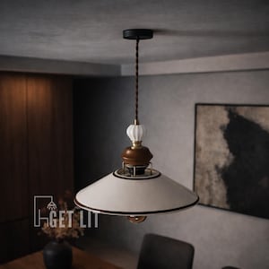 May include: A pendant light fixture with a white, bell-shaped shade, accented with brown trim and a brass-colored rim. The fixture has a brown and white decorative top and a black ceiling mount. The text "GET LIT" is visible on the lower left.