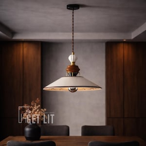 May include: A pendant light fixture with a cream-colored shade and a decorative wooden and ceramic top. The light hangs from a brown cord and has a black ceiling mount. The image also shows a table, chairs, and the text "GET LIT".