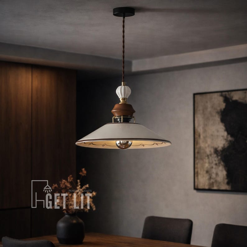 May include: Cream-colored pendant light with a decorative design. The light fixture has a white shade with a gold interior and a brown and white decorative top. The light is suspended from a brown cord. The text "GET LIT" is visible.