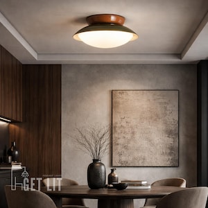May include: A modern ceiling light with a brown top and a green, bowl-shaped shade. The light has a frosted glass diffuser. The fixture is installed in a dining room with a dark wood table and chairs.