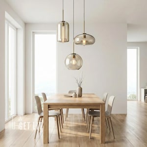Puede incluir: Tres lámparas colgantes modernas con pantallas de vidrio transparente y herrajes color latón cuelgan sobre una mesa de comedor de madera. Las pantallas tienen diferentes formas: un cilindro, un óvalo aplanado y una esfera. La habitación tiene un diseño minimalista.