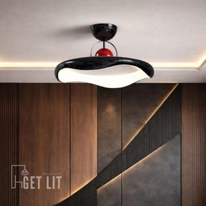 Peut inclure: Un luminaire suspendu moderne avec un extérieur noir brillant et un intérieur blanc ondulé. Une sphère rouge et un dôme noir sont au-dessus de la lumière principale. Le texte "GET LIT" est visible en bas à gauche.