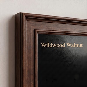 May include: A dark brown wooden picture frame with a stepped profile edge. The frame surrounds a black surface featuring the text Wildwood Walnut in a light tan, sans-serif font. The wood grain is visible on the frame's surface.