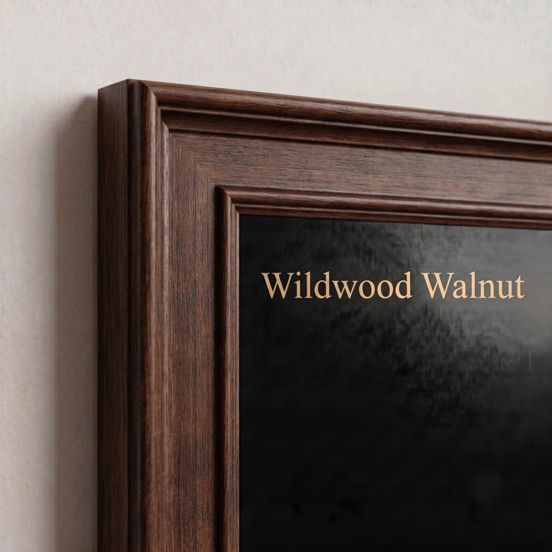 May include: A dark brown wooden picture frame with a stepped profile and a visible wood grain texture. The frame surrounds a black surface featuring the light tan text Wildwood Walnut printed in a clean, sans-serif font on the upper portion.