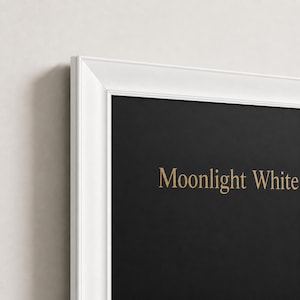 May include: A white picture frame with a beveled edge surrounding a solid black background. The text Moonlight White is printed in a gold serif font on the black surface. The frame has a clean, simple design with a smooth matte finish.