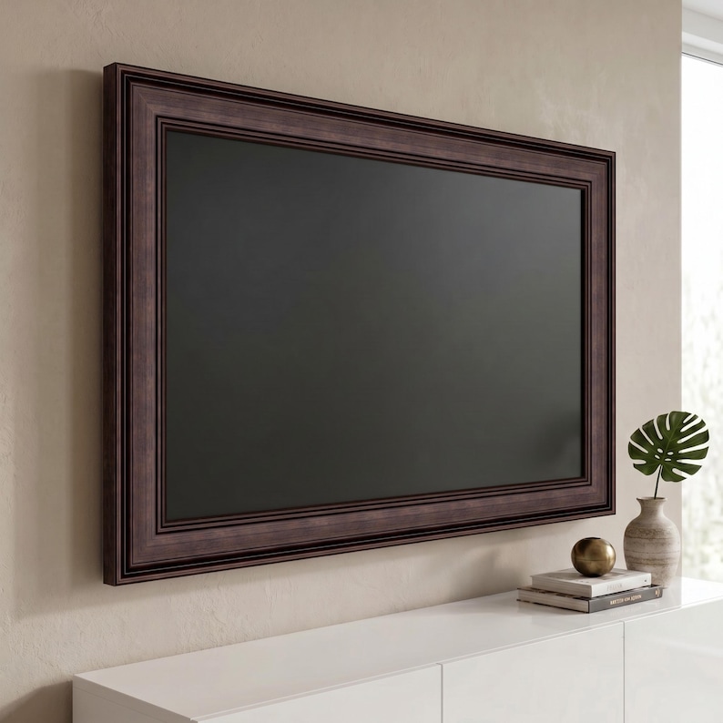 May include: A rectangular television screen mounted on a wall, encased in a dark brown wooden frame with a multi-layered, stepped profile. The screen is black and inactive, displaying a flat, dark surface within the decorative, textured border.