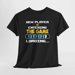 May include: Black t-shirt featuring the text "NEW PLAYER IS ENTERING THE GAME" in white and yellow. A loading bar with blue footprints is below the text. This t-shirt is designed for casual wear.