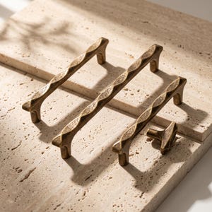 May include: Three elongated metal cabinet pulls and one small matching cabinet knob, all featuring a textured, hammered surface with a dark antique brass finish. The hardware pieces have a distinct faceted design along the length of the pulls.