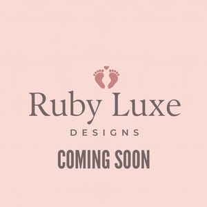 May include: A light pink background with the text "Ruby Luxe Designs" in a dark gray font. Below the text is "COMING SOON" in a bold, dark gray font. The image also includes a graphic of two baby footprints with a heart and the text "LAUNCHING IN 2026".