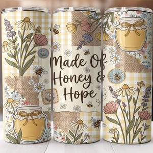 Puede incluir: Un juego de tres vasos de acero inoxidable con un diseño floral y de abejas. Los vasos presentan un patrón de patchwork con margaritas, lavanda y tarros de miel. El texto "Made Of Honey & Hope" se muestra en el vaso central.