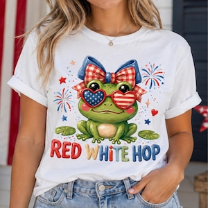 Könnte beinhalten: Weißes T-Shirt mit einer Cartoon-Froschfigur, die eine patriotische Sonnenbrille und eine Schleife trägt. Der Frosch ist grün mit roten, weißen und blauen Akzenten. Der Text "RED WHITE HOP" wird in bunten Buchstaben darunter angezeigt.