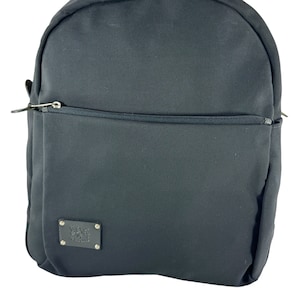 May include: Black backpack with a zipper closure and a small leather patch with a logo on the front.