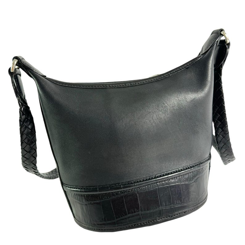 May include: Black leather shoulder bag with a braided strap. The bag has a cylindrical shape with a textured bottom section. The strap is attached with silver-colored hardware.