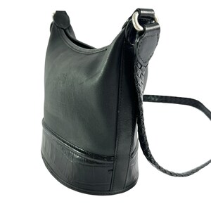 May include: Black leather shoulder bag with a braided strap and silver-tone hardware. The bottom of the bag has a textured, crocodile-like pattern. The bag is designed to be worn over the shoulder.