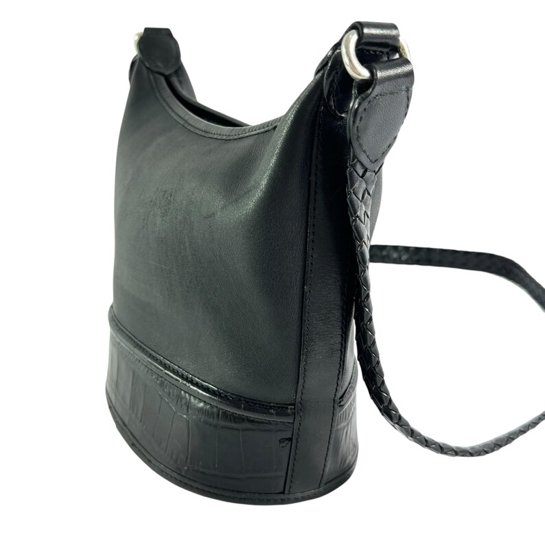 May include: Black leather shoulder bag with a braided strap and silver-tone hardware. The bottom of the bag has a textured, crocodile-like pattern. The bag is designed to be worn over the shoulder.