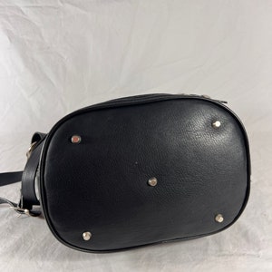 Puede incluir: Bolso de cuero negro de estilo cubo con detalles en metal plateado. El bolso tiene un fondo redondeado y cierre de cremallera.