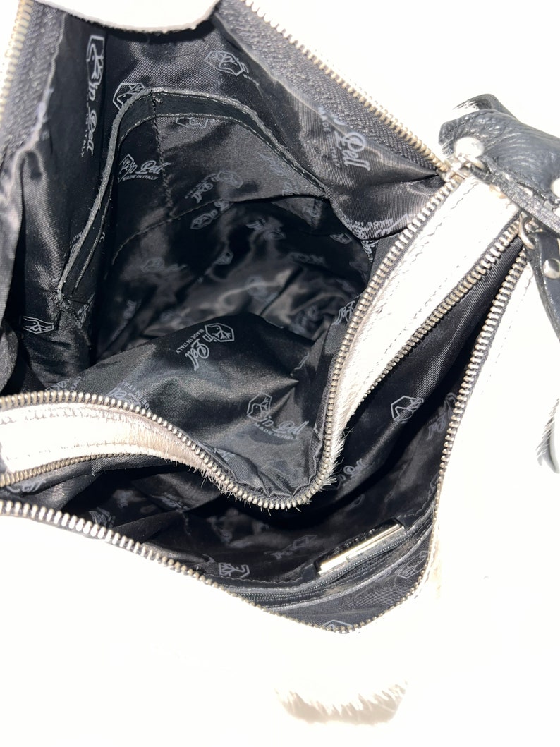 Puede incluir: Bolso de mano de cuero blanco con cremallera negra y forro negro. El forro tiene un logotipo repetido de una mano estilizada sosteniendo un coraz&oacute;n.
