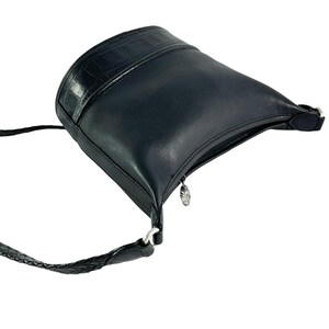 May include: Black leather shoulder bag with a textured top panel and a braided strap. The bag has a silver zipper pull and hardware. The bag is angled, showing the shape and details of the design.