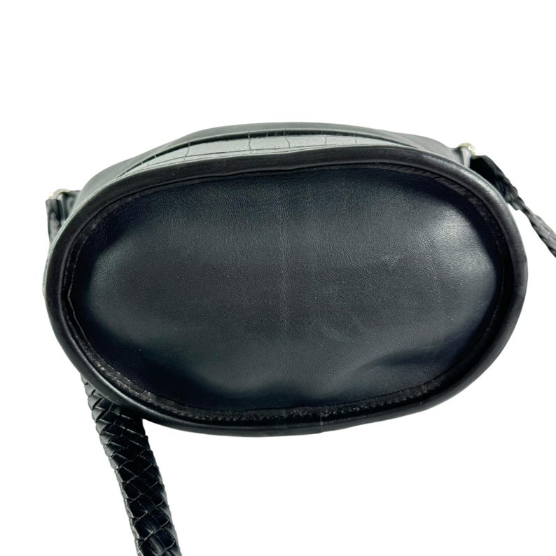 May include: Black leather crossbody bag with a textured crocodile-like pattern on the top. The bag has a braided strap and a rounded bottom. The bag is designed to be worn over the shoulder or across the body.