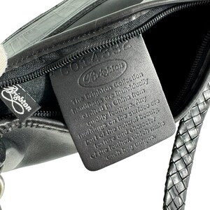 May include: Black leather Brighton handbag with a braided strap and a zipper. The Brighton logo is visible on a tag and the bag itself. The tag reads "The Brighton Collection handbags are individually crafted in China from quality leathers."