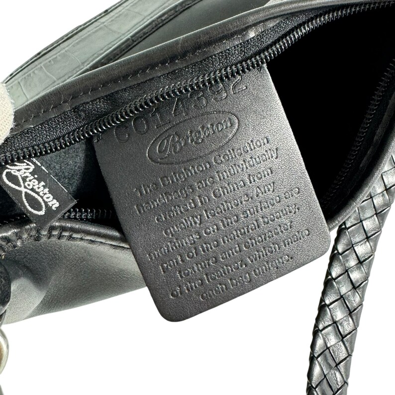 May include: Black leather Brighton handbag with a braided strap and a zipper. The Brighton logo is visible on a tag and the bag itself. The tag reads "The Brighton Collection handbags are individually crafted in China from quality leathers."