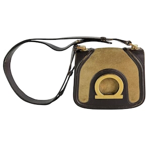 May include: A brown leather shoulder bag with a gold-colored clasp and a suede front panel. The bag features a gold-colored metal emblem and a long, adjustable strap. The bag is rectangular in shape.