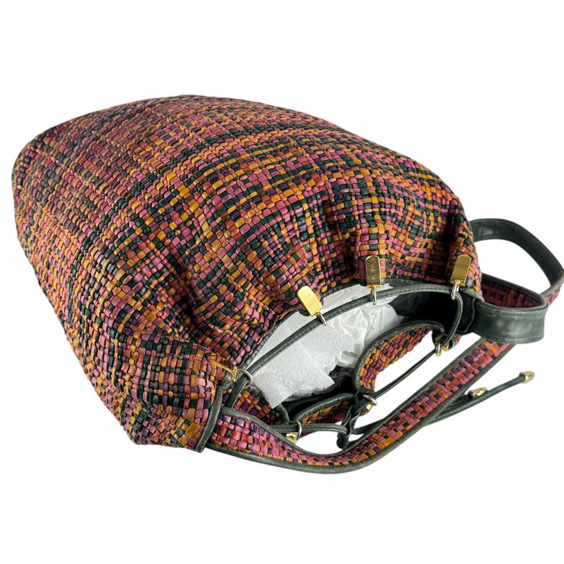 May include: A woven handbag in shades of pink, orange, and black. The bag has a drawstring closure and black leather straps with gold-tone hardware. The interior is lined with white fabric.