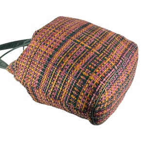 May include: A colourful woven tote bag featuring a pattern of pink, yellow, and green. The bag has a rectangular shape with dark green trim and handles. The weave is tight, suggesting a sturdy construction.