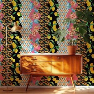 May include: A mid-century modern wooden sideboard with three drawers and a cabinet door, positioned against wallpaper featuring a geometric pattern of lemons, flowers, and blue and white pottery. A brass floor lamp and a potted monstera plant.