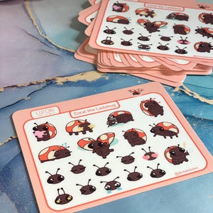May include: A rectangular sticker sheet featuring multiple small illustrations of a brown ladybug with orange spots, labeled Coral the Ladybug and LUFORi. The sheet includes various expressions and poses, such as sleeping, crying, and holding hearts.