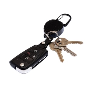 May include: A black key fob with several keys attached. The key fob has buttons and a silver trim. A black retractable reel with a carabiner clip is attached to the key fob. The keys are silver and have different shapes.