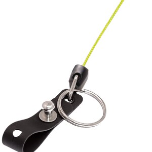 May include: A black leather keychain strap with a silver metal split ring and a silver rivet. A neon green cord extends from a black plastic connector attached to the split ring.