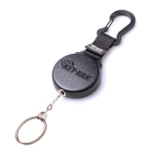 May include: Black KEY-BAK retractable key holder with a carabiner clip. The round, textured holder has the KEY-BAK logo and a steel key ring attached by a chain. The clip and holder are connected by a black nylon strap.