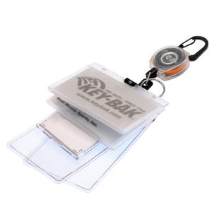 May include: A clear plastic Key-Bak ID holder with a retractable reel and a black carabiner clip. The holder has a stack of clear plastic card sleeves. The Key-Bak logo and website are visible on the top card.