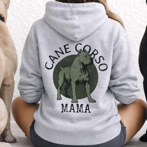 May include: A light grey hoodie with the text "CANE CORSO MAMA" and a Cane Corso dog graphic. Two Cane Corso dogs, one tan and one black, sit either side of the person wearing the hoodie.