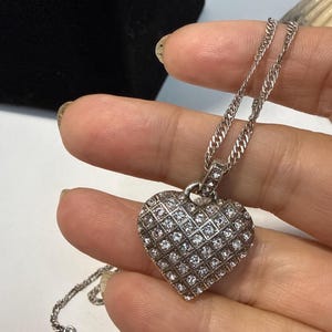Puede incluir: Un collar con colgante de coraz&oacute;n plateado. El colgante en forma de coraz&oacute;n est&aacute; cubierto de peque&ntilde;as piedras claras y brillantes dispuestas en un patr&oacute;n de rejilla. La cadena del collar es de estilo eslabones finos, con un cierre a juego.