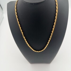 May include: A gold-toned chain necklace featuring a series of interconnected, leaf-shaped or petal-like links. The necklace has a polished, reflective surface and a continuous, uniform design that forms a circular shape around the neck display.