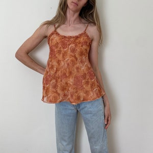 May include: A sleeveless, orange floral print top with a ruffled neckline. The top is made of a sheer fabric and has a relaxed fit.