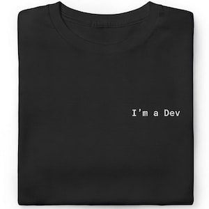 May include: Black t-shirt with the text "I'm a Dev" in white, centered on the chest. The shirt is folded neatly, showcasing its simple design. The bottom right corner has a black tag that says "Black".