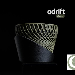 Könnte beinhalten: Ein dekorativer Pflanzentopf mit einem einzigartigen Design. Der Topf hat ein gitterartiges Muster in Olivgrün, das von einem schwarzen Sockel getragen wird. Das Wort "adrift" wird über dem Topf angezeigt, darunter das Wort "planter".