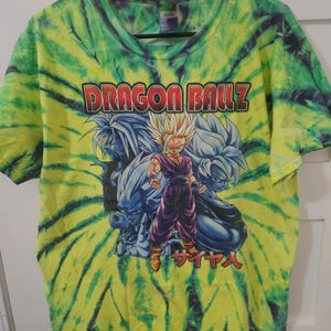 May include: A tie-dye t-shirt with a vibrant green and yellow spiral pattern. The front features the text "DRAGON BALL Z" above a graphic of anime characters. The Japanese word "Saiyan" is also visible.