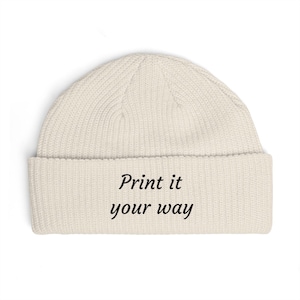 May include: Cream-colored beanie with a ribbed knit texture. The folded brim displays the text "Print it your way" in a black, sans-serif font. The hat is a neutral color, suitable for various outfits.