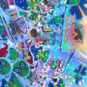 May include: A collection of holographic stickers featuring various designs including frogs dressed as wizards in blue robes with star patterns, a knight in armour holding a shield, red hearts, and green alien faces. The stickers have a reflective finish.