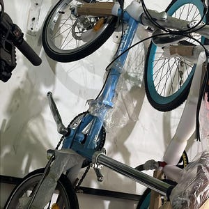 Könnte beinhalten: Ein hellblaues Klappfahrrad mit schwarzen Reifen und silbernen Felgen. Das Fahrrad hat einen blauen Rahmen und ist teilweise in Schutzplastik verpackt. Die Räder haben einen Durchmesser von ca. 51 cm.